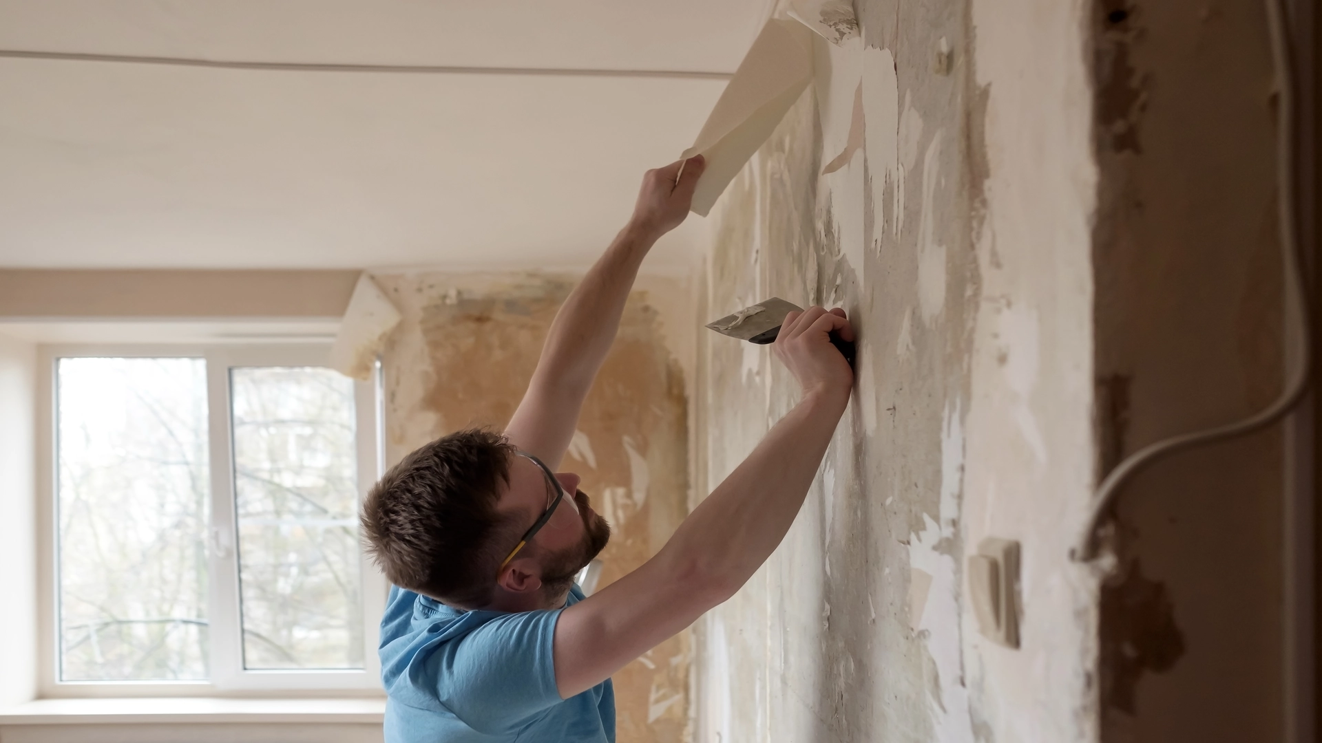 hardworking-man-removes-old-wallpaper-from-wall